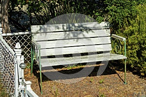 Aged and weathered wooden bench with small metal chain link fence and green hand rails with wood chip floor and shrubs