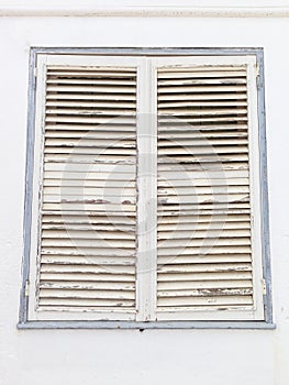 Aged white closed window shutters with peeling paint