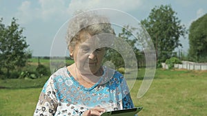 Aged woman 80s holding a digital tablet outdoors