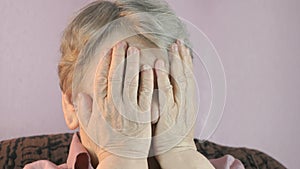 Aged woman 80s sitting indoors covers face hands