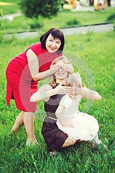 Aged woman with adult daughter and little granddaughter have fun toghether outdoor, close eyes to each other.