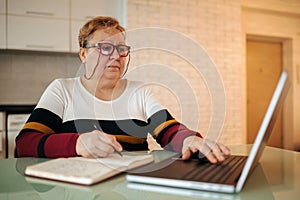 An aged woman with eyeglasses and a laptop uses technology for information and knowledge acquisition