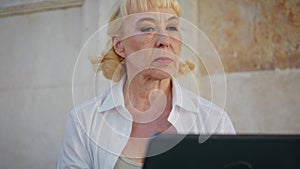 Aged woman freelancer working laptop on street closeup. Portrait of elderly lady