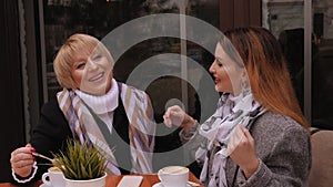 Aged woman and her adult daughter drinking coffee at sidewalk cafe in spring.