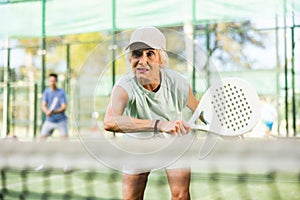 Aged woman hitting ball with backhand during paddleball match on outdoor court