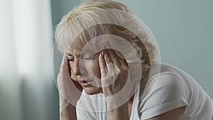 Aged woman rubbing temples intensely, splitting headache, problems with health