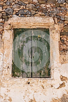 Aged wooden closed shutters, peeled stone wall building facade, green window planks. Vertical