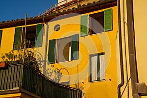 Aged yellow structure featuring green window shutters in Italy