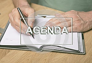 Agenda word. Inscription on photo of hands writing in planner or organizer