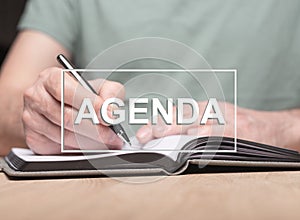 Agenda word with photo of male hands writing in planner or organizer