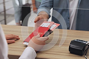 Agent giving passports with tickets to client at check-in desk in airport, closeup