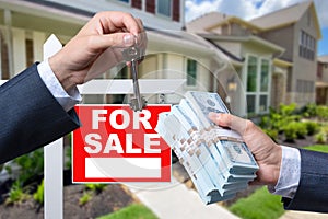 Agent Handing Over Keys as Buyer is Handing Over Cash for House with Home and For Sale Real Estate Sign Behind.