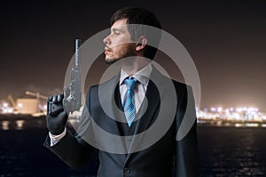 Agent or hitman holds pistol with silencer in hand at night