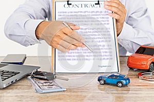 The agent`s hand holds a pen pointing to the document to have signed the rental form. The idea of selling a car with car insurance