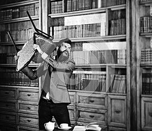 Aggression, hate, nervous, negative emotions concept. Man with angry face holds chair and ruins library. Bearded man in