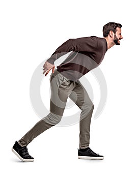 An aggressive bearded man in casual garb stands in a side view and growls or shouts at something.