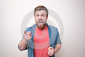 Aggressive bearded man yells and reproaches someone, he looks viciously, points his finger and blames. White background.