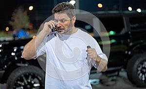 Aggressive brutal man talking on phone outdoor. Hipster guy talking on phone near car on night city street. Serious man