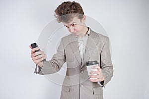 Aggressive caucasian teenager screams into the smart phone and holds a paper cup of coffee in his hand. student on edge on a white