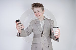 Aggressive caucasian teenager screams into the smart phone and holds a paper cup of coffee in his hand. student on edge on a white