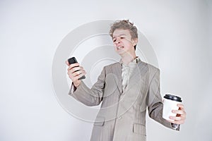 Aggressive caucasian teenager screams into the smart phone and holds a paper cup of coffee in his hand. student on edge on a white