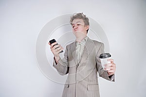 Aggressive caucasian teenager screams into the smart phone and holds a paper cup of coffee in his hand. student on edge on a white