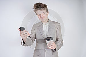 Aggressive caucasian teenager screams into the smart phone and holds a paper cup of coffee in his hand. student on edge on a white