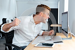 Aggressive furious businessman shouting and working with computer in office