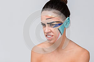 An aggressive girl, with bare shoulders and with a colorful creative geometric greasepaint on her face.