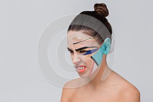 An aggressive girl, with a geometric greasepaint on her face grimaces.