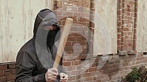 Aggressive hooligan in mask and hood ganging with baseball bat, crane shot
