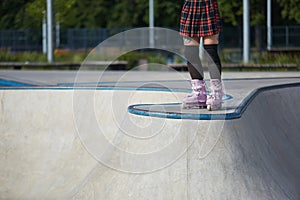 Aggressive inline skater girl wearing modern roller blades and protective knee pads and shin guards in a concrete skatepark. Cool
