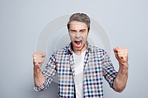 Aggressive man in checkered shirt with raised fists and open mouth is out of himself, yelling, screaming, shouting with cruelty o