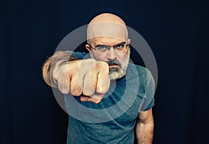 Aggressive man with gray beard punches at camera on black background