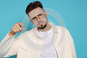 Aggressive man in white jacket and eyeglasses pointing finger on light blue background