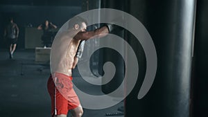 Aggressive professional fighter is training with a punching bag, inflicting a furious blow. The champion is engaged in