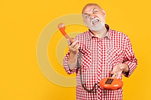 aggressive senior man with retro telephone on yellow background