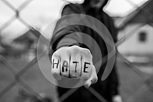 Aggressive teenage boy showing hes fist behind wired fence at the correctional institute, the word hate is written on hes hand