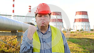 Aggressive worker looking directly at the camera and threatening with his fist, standing in front of a power station