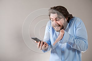 Aggressive young business man in blue shirt shouting into his mobile phone on grey