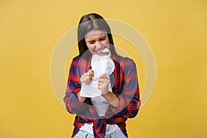 Aggressive young caucasian woman tears contract or white sheet of paper. Isolated over yellow background.