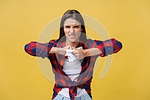Aggressive young caucasian woman tears contract or white sheet of paper. Isolated over yellow background.
