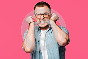 aggressive young man in eyeglasses biting handcuffs and looking at camera isolated