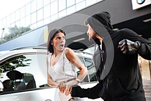 Aggressive young man thief in hoodie robbing scared woman