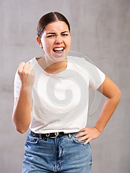 Aggressive young woman standing against unicoloured background