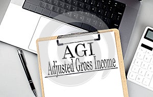 AGI -ADJUSTED GROSS INCOME word on clipboard on laptop with calculator and pen photo