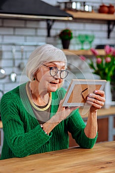 Aging lady lovingly looking at picture sitting at kitchen table