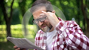 Aging man in eyeglasses trying to read newspaper in park, farsightedness, myopia