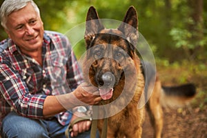 Aging man posing with his german shepherd in the woods