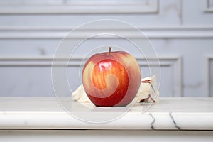 aging red apple with a bruised side on a marble surface